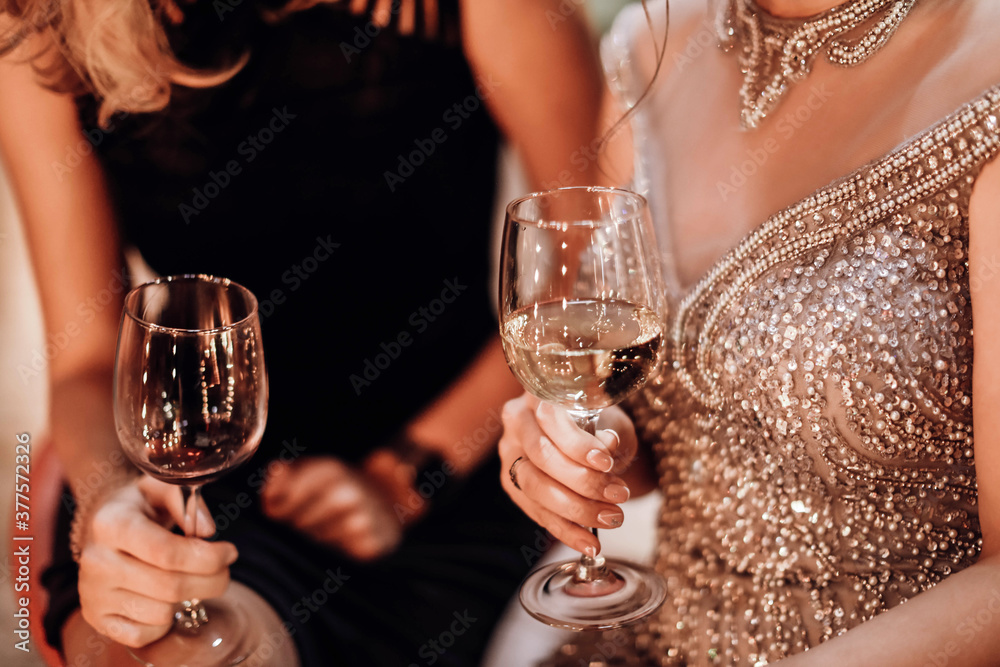 Hands of women in evening beautiful dresses with glasses of red and white wine celebrating and toasting