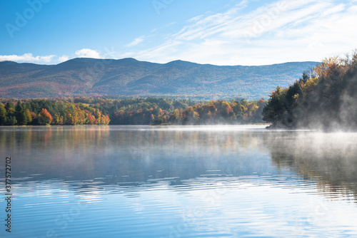 Morning fog drifting over the water of mountain lake with wooded shores at the peak of fall foliage. Waterbury  VT  USA.