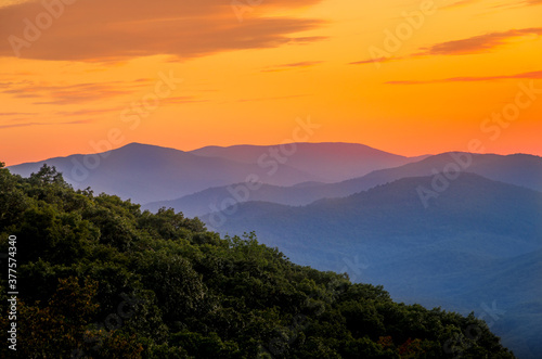 Blue mountains fading into the distance against an orange sunset © Scott
