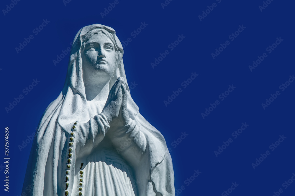 Obraz premium Virgin Mary ancient statue against blue background of sky.