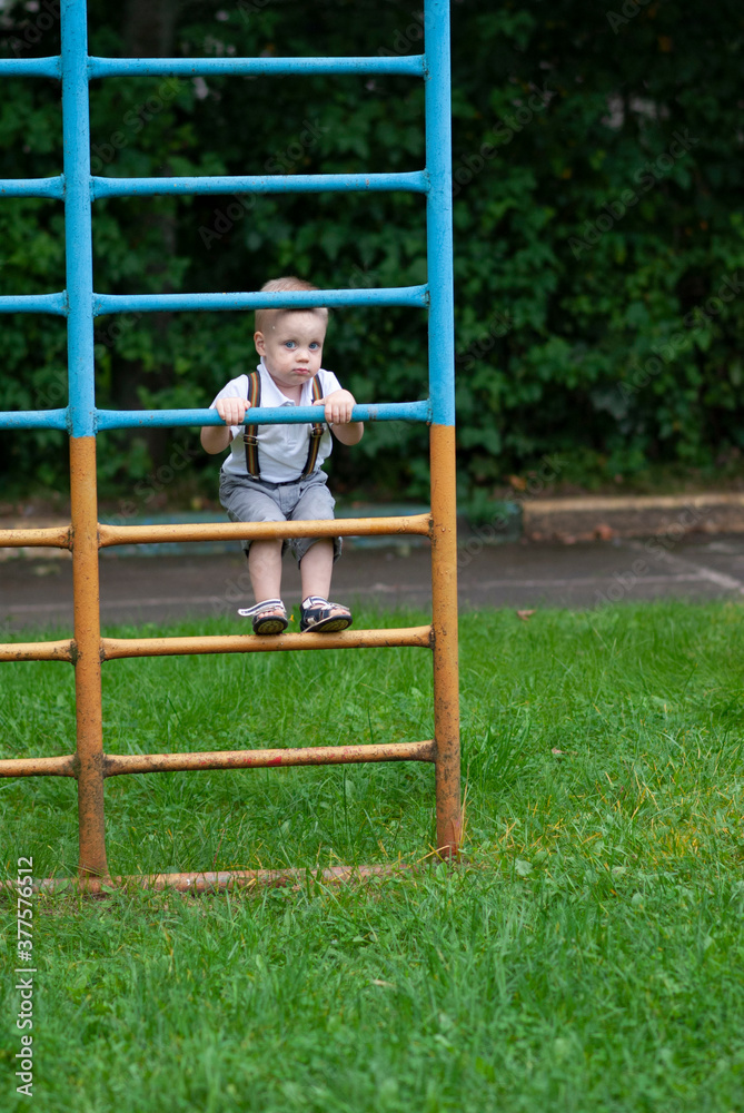 A little boy climbed the gymnastic ladder and peeps between the bars A little boy climbed the gymnastic ladder and peeps between the bars