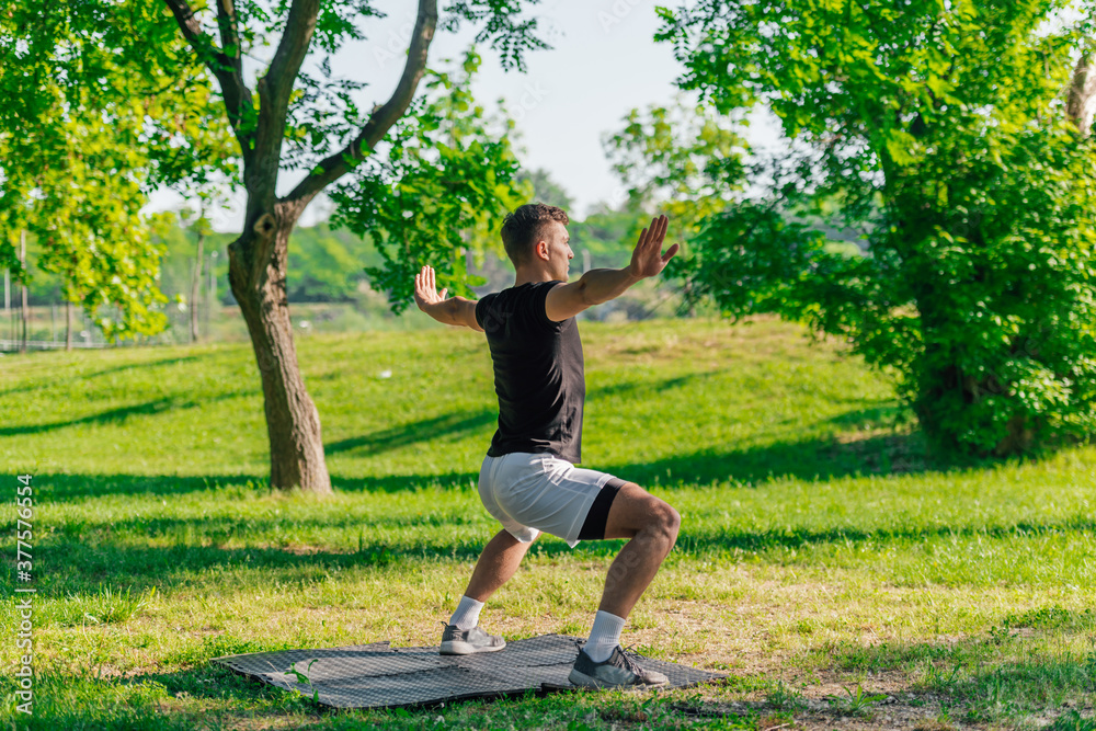 A young man practices yoga with the variations of the goddess pose outdoor in the park A young man practices yoga with the variations of the goddess pose outdoor in the park