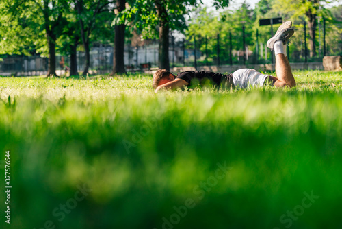 Athletic sportsman laying on the green grass and resting from a workout in the park
