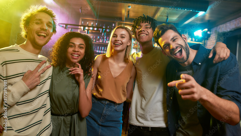 Dream Team. Portrait of young men and women looking at camera and smiling. Multiracial group of friends hanging out at party in the bar