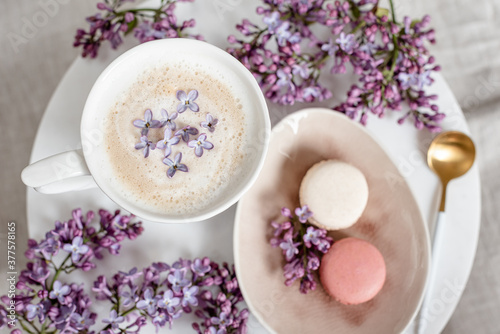 Cappuccino with macaroons on linen tablecloth, violet lilac flowers, morning concept