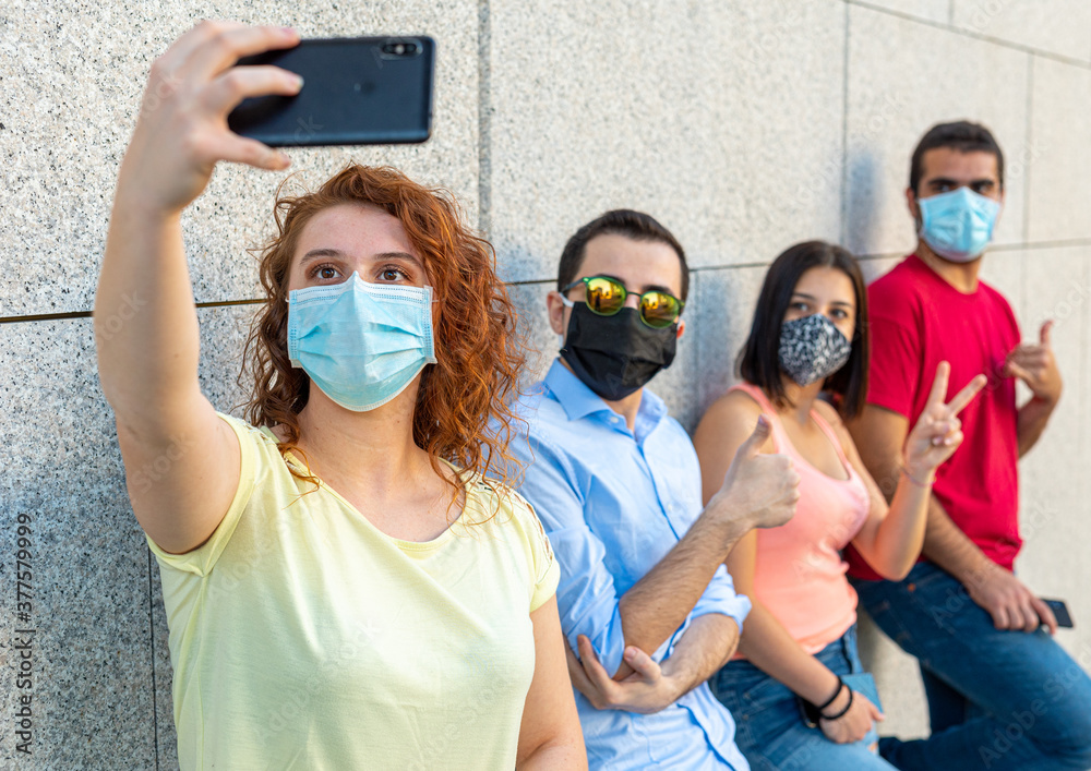 group selfie, young girls and boys in a row leaning against a wall take pictures with protective masks,  focus on the girl with red hair, new normal concept