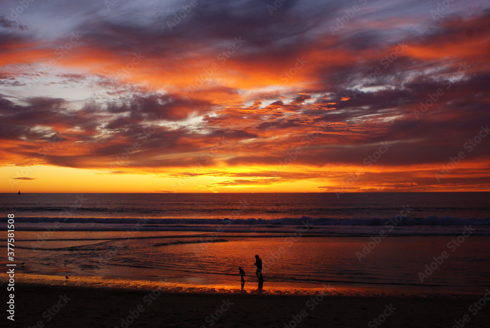Parent and child walk along beach at sunset