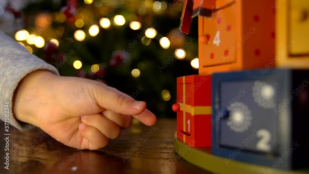 Close up of child hand opening advent calendar wooden door and finding a surprise gift. 
