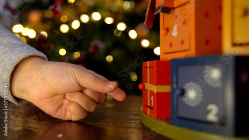 Close up of child hand opening advent calendar wooden door and finding a surprise gift. 
