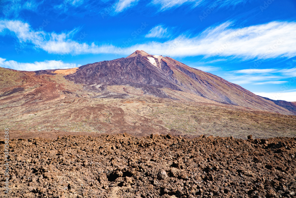 View of the Teide volcano from the valley of the geological park. Volcanic stone with purple pigments and blue sky in the background.