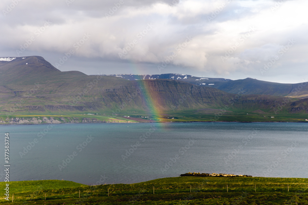 rainbow over a lake with green hills behind on a cloudy day