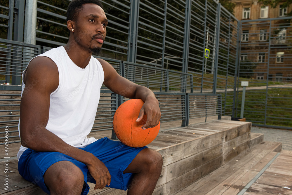 Young african american basketball player in white t-shirt and blue shorts  on basketball court sitting, holding basketball, conceived, sport concept  Stock 写真 | Adobe Stock