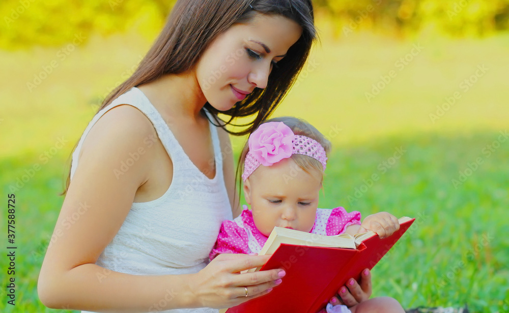 Close up portrait of mother with baby reading book sitting together on the grass outdoors Close up portrait of mother with baby reading book sitting together on the grass outdoors