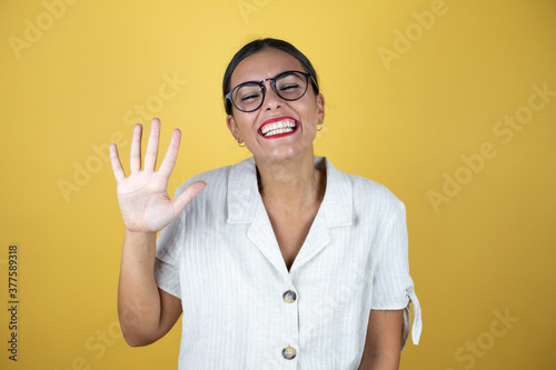 Beautiful woman over yellow background showing and pointing up with fingers number five while smiling confident and happy.