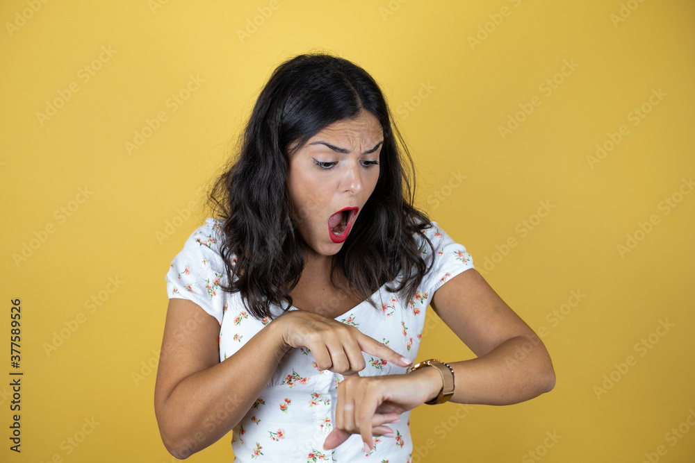 Obraz premium Beautiful woman over yellow background surprised and pointing his watch because it's late
