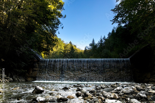 renewable energy, barrage of a wild river, flowing water with a bed of gravel stones, framed  by green trees