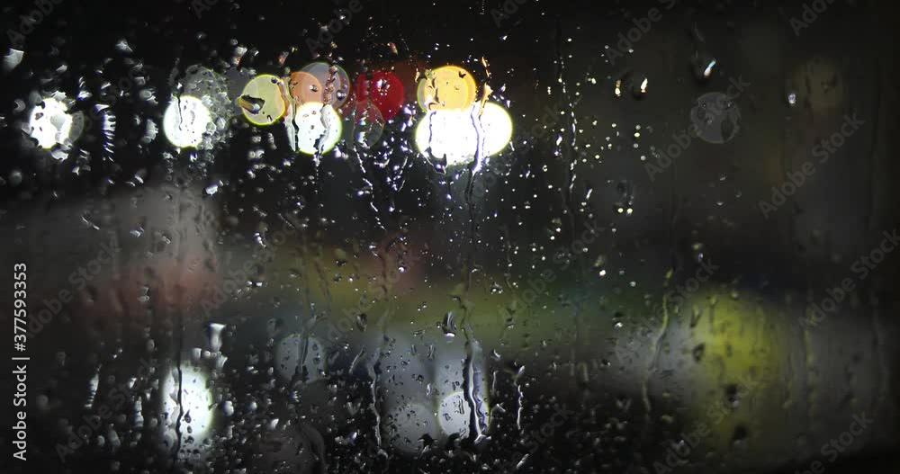 Timelapse video of drops of night rain on the window and blurred backlight