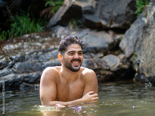 Hombre joven disfrutando de sus vacaciones de verano bañándose en un lago con rocas y una catarata en el fondo. Situado en Bali, Indonesia