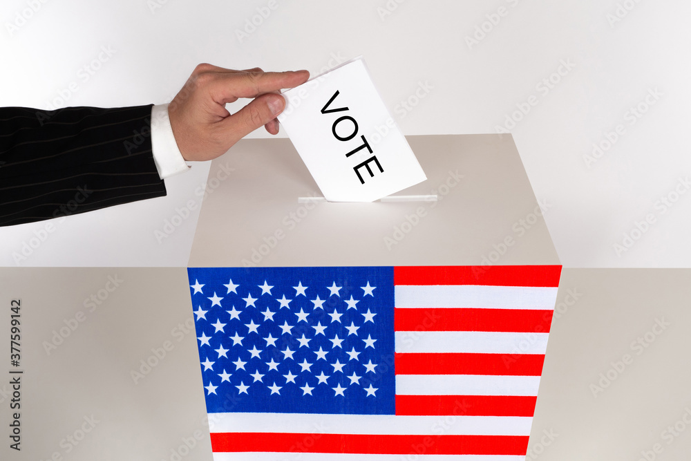Man voting on elections of the President of the United States. A man hand drops his ballot into the ballot box. Americans choose their President. Voting box in the colors of the USA flag. Man voting on elections of the President of the United States. A man hand drops his ballot into the ballot box. Americans choose their President. Voting box in the colors of the USA flag.