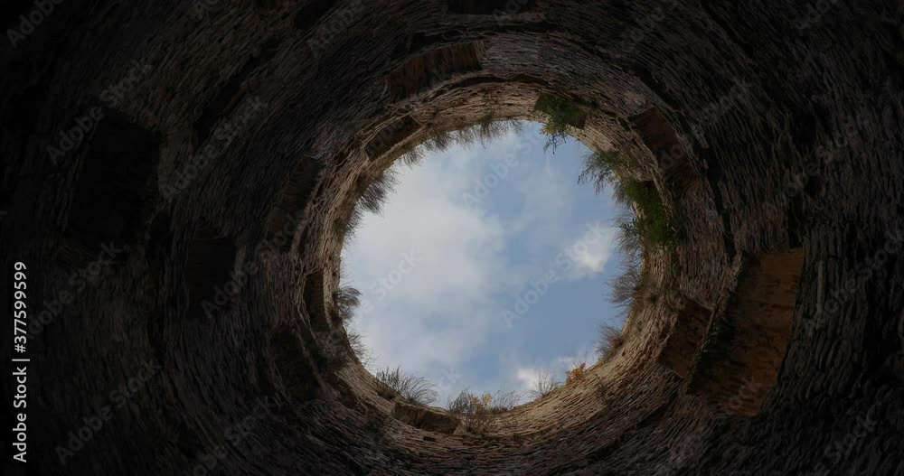 A view of the blue sky with running clouds from bottom to top of abandoned ancient medieval castle tower.