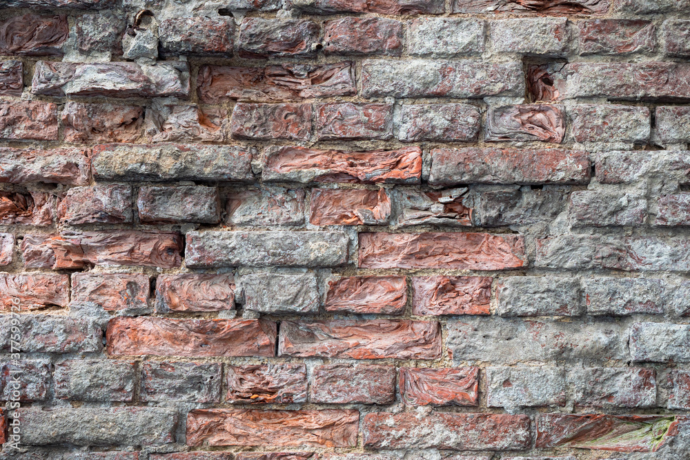 Obraz premium Geometric background made of old bricks. The brick wall is gray-brown. The surface of crumbling bricks.