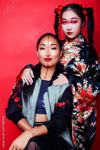 two pretty geisha girls friends: modern asian woman and traditional wearing kimono posing cheerful on red background © iordani