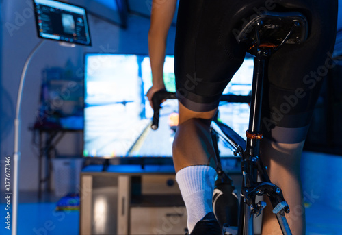 Asian man cycling on the machine trainer he is exercising in the home at night.he play online bike game