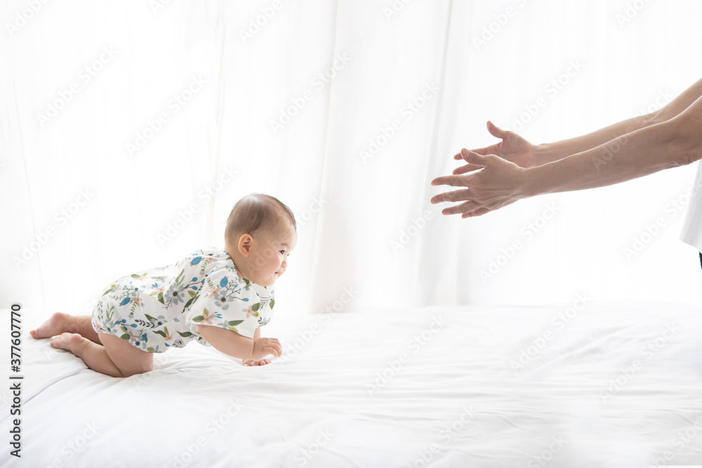 Asian Baby Crawling on the Bed to her Mother Hand