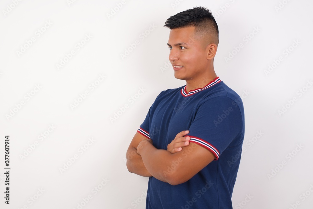 Portrait of cheerful lovely Young handsome hispanic man wearing casual t-shirt standing over white isolated background crossing arms looking aside having a nice conversation Portrait of cheerful lovely Young handsome hispanic man wearing casual t-shirt standing over white isolated background crossing arms looking aside having a nice conversation