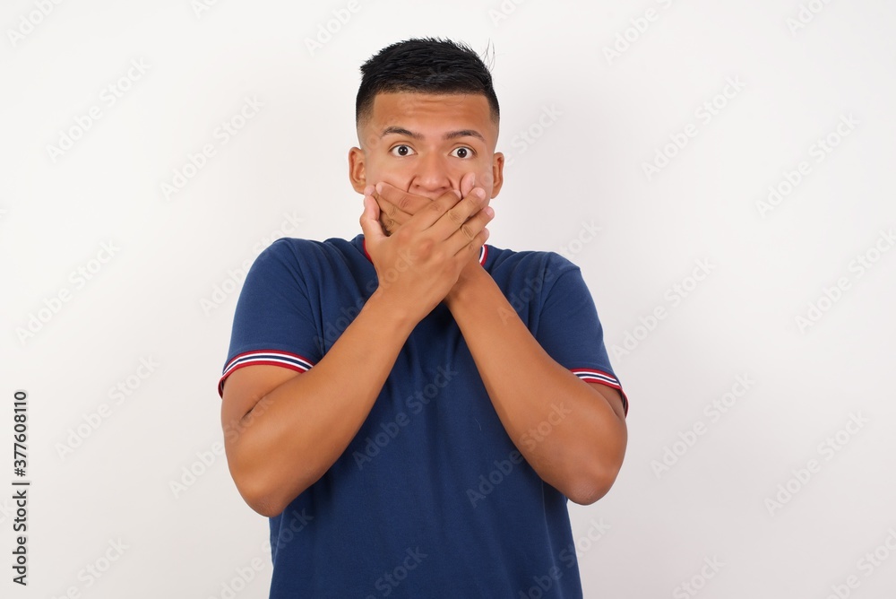 Young handsome hispanic man wearing casual t-shirt standing over white isolated background shocked covering mouth with hands for mistake. Secret concept. Young handsome hispanic man wearing casual t-shirt standing over white isolated background shocked covering mouth with hands for mistake. Secret concept.