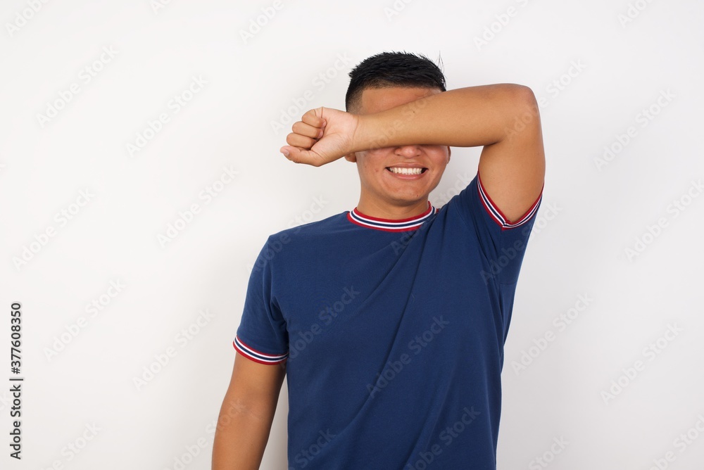 Young handsome hispanic man wearing casual t-shirt standing over white isolated background covering eyes with arm smiling cheerful and funny. Blind concept. Young handsome hispanic man wearing casual t-shirt standing over white isolated background covering eyes with arm smiling cheerful and funny. Blind concept.