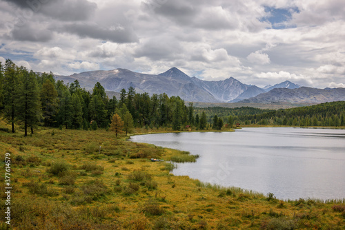 Quiet lake among the mountain peaks and pine forests, cloudy sky. Idyllic panorama of autumn, Alpine landscape.