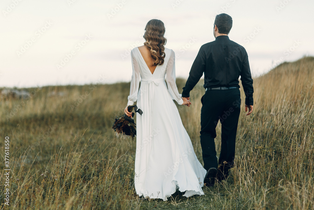 A beautiful fairy-tale happy bride with a bouquet and a wreath and a stylish groom on the background of rocks in the mountains. Boho wedding in nature. A beautiful fairy-tale happy bride with a bouquet and a wreath and a stylish groom on the background of rocks in the mountains. Boho wedding in nature.