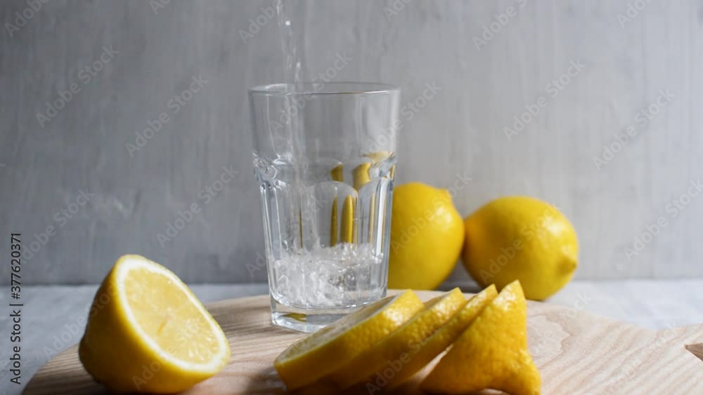 Chef pouring water and squeeze juice from fresh lemon into glass. Close-up. Lemon water. Healthy, dietary nutrition.