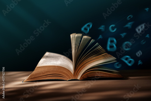 Reading, Education, Learning Concept. Manipulation Photo of Opened Book  with Blowing Alphabet on Table