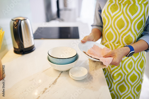 Cropped image of woman wiping dishware with cotton towel in kitchen