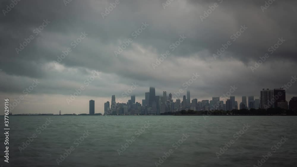 Panoramic city skyline view time lapse of Chicago with dramatic storm clouds in the sky moving over the water of Lake Michigan at sunset as day turns to night and building lights turn on downtown. Panoramic city skyline view time lapse of Chicago with dramatic storm clouds in the sky moving over the water of Lake Michigan at sunset as day turns to night and building lights turn on downtown.