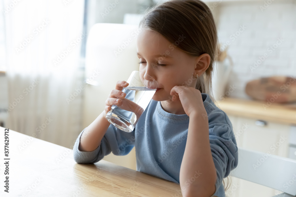 Head shot thirsty small cute caucasian kid girl sitting at table, drinking fresh cool stilled clear water, preventing dehydration at home, happy little child enjoying healthcare routine in kitchen. Head shot thirsty small cute caucasian kid girl sitting at table, drinking fresh cool stilled clear water, preventing dehydration at home, happy little child enjoying healthcare routine in kitchen.