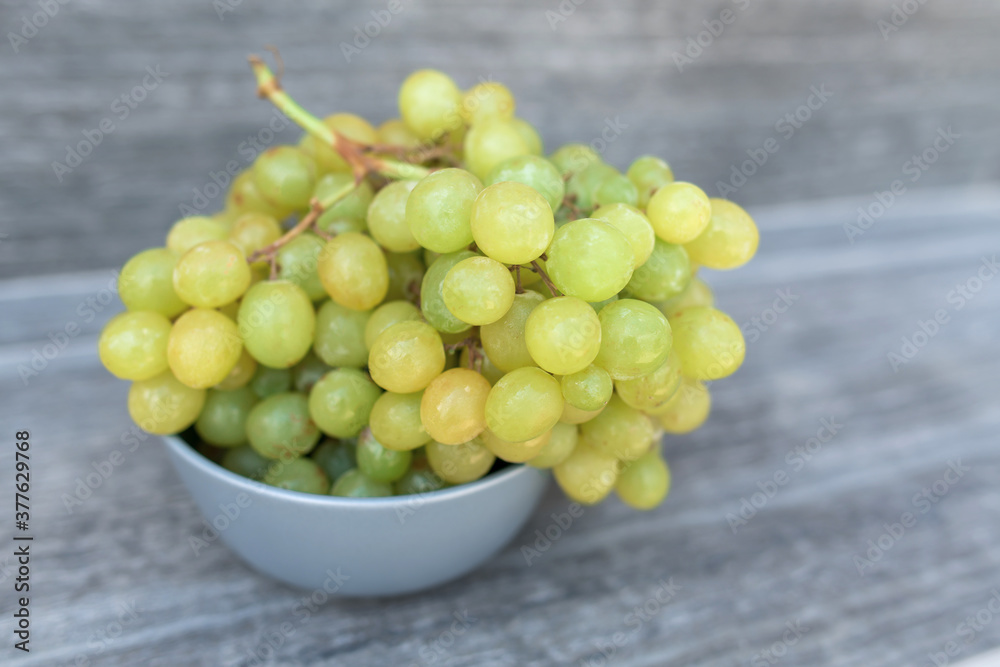 A bunch of ripe green grapes in a gray plat on a gray background. A bunch of ripe green grapes in a gray plat on a gray background.