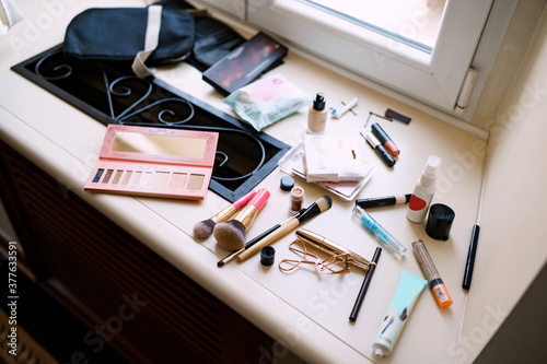 Makeup artist set. Eyeshadow palette, makeup brushes, mascara and eyelash curler on the windowsill by the window.