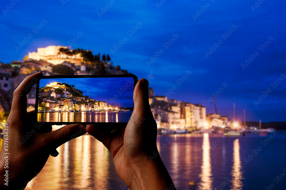 Φωτογραφία Tourist taking photo of illuminated Sibenik with fortress, old buildings, sea and blue sky