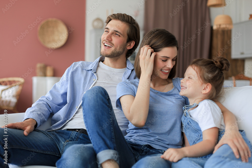 Positive friendly young parents with smiling little daughter sitting on sofa together while relaxing at home on weekend. Positive friendly young parents with smiling little daughter sitting on sofa together while relaxing at home on weekend.