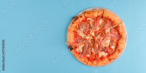 Whole Italian pizza with cheese and mushrooms on a metal tray over bright blue pastel bakcground.