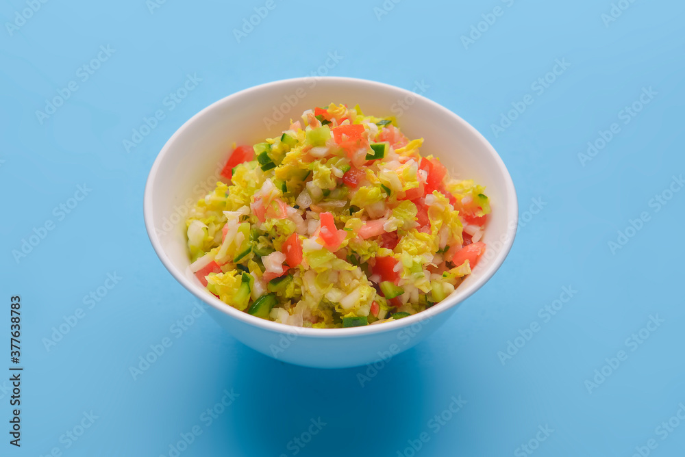 Fresh vegetables and green salad served in a bowl over pastel blue background. Healthy eating concept.
