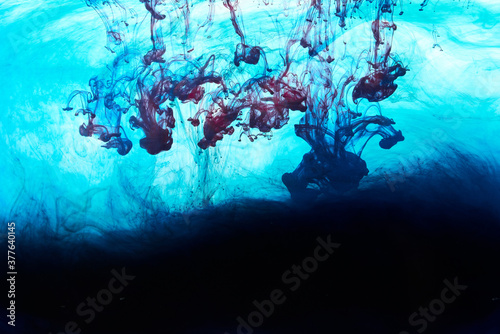 Closeup of a blue, black and red ink in water in motion isolated on white. Ink swirling underwater. Colored abstract smoke explosion effect. Abstract background with copy space..