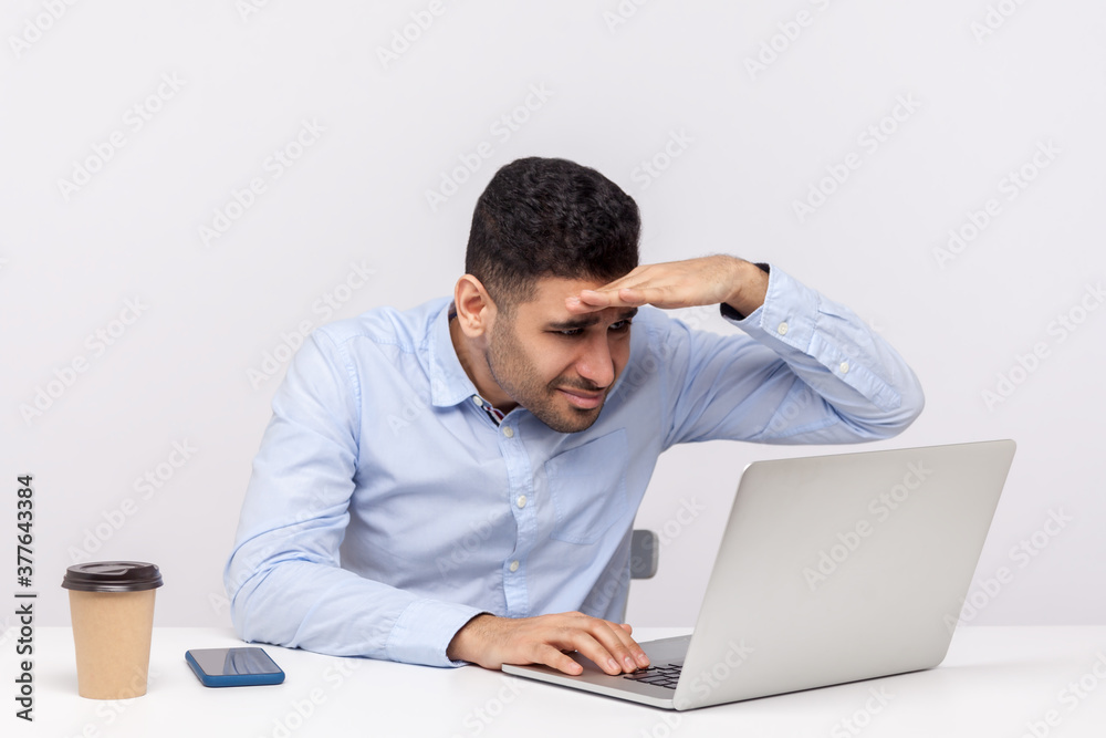 Computer vision syndrome. Male office employee working on laptop and carefully looking at screen, keeping hand over eyes focusing at display, having eyesight problems. indoor studio shot isolated Computer vision syndrome. Male office employee working on laptop and carefully looking at screen, keeping hand over eyes focusing at display, having eyesight problems. indoor studio shot isolated