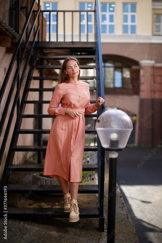Obraz premium Outdoor portrait of young smiling Caucasian woman near to black metal ladder. city portrait