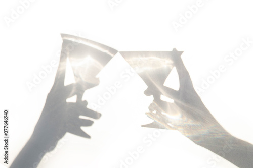 Contrasting shadow two hands with glasses make on cheers a white background. Holiday concept
