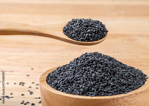 Close-up macro shot wooden spoon to scoop black sesame seeds from a wooden bowl on table wood background, organic  food concept.