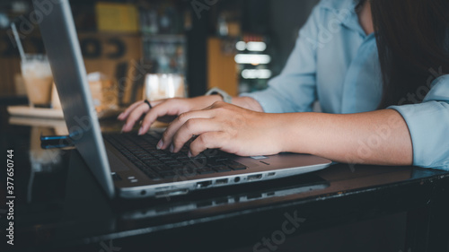 A female Asian office worker of Thai descent is typing and working with notebooks in a coffee shop during the day. She was wearing a blue shirt